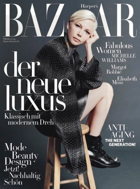 Michelle Williams poses on a stool for Harper's Bazaar cover. She wears a patterned jacket, black skirt, and boots against a grey backdrop.