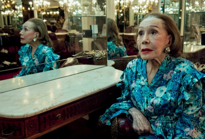 Elderly woman in a blue floral dress seated next to a vintage vanity mirror in Los Angeles photographed by Sofia and Mauro