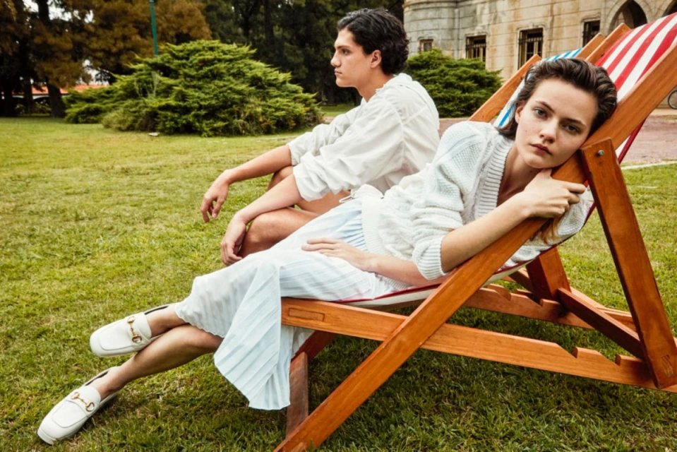 Two people in a lawn setting: one woman lying on a red and white striped deckchair and one man sitting in the background.