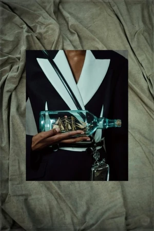 Person in blazer holding a ship-in-a-bottle against a draped fabric backdrop, creating an unusual and eye-catching presentation.