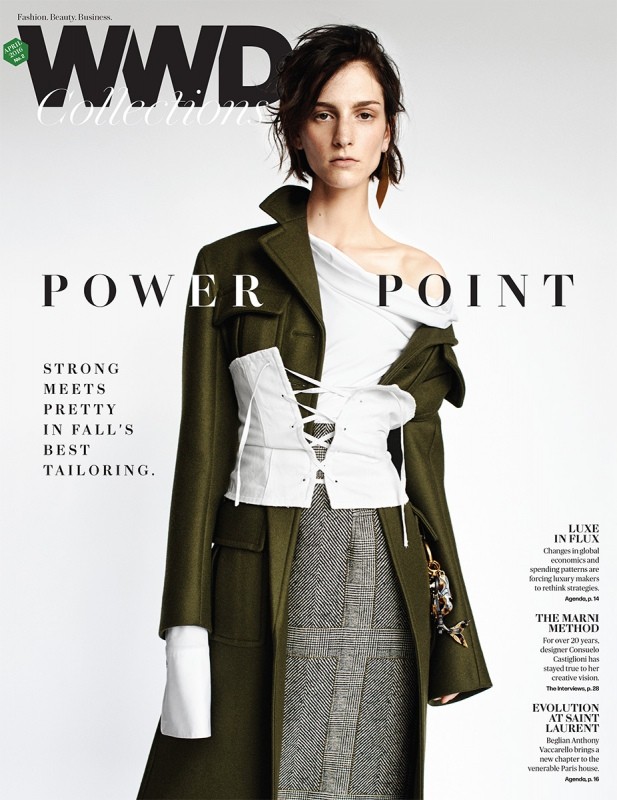 Fashion editorial magazine cover featuring a model in a draped white top, plaid skirt, and green coat against a neutral backdrop.