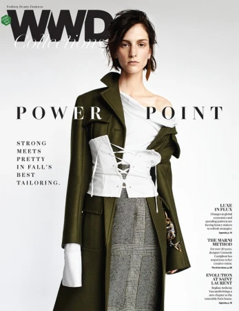 Fashion editorial magazine cover featuring a model in a draped white top, plaid skirt, and green coat against a neutral backdrop.