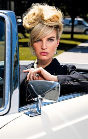 Model with voluminous blonde updo hairstyle sitting in a white convertible car