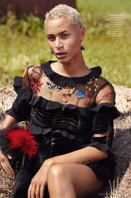 Portrait of a young woman with short blonde hair, adorned with floral dress, seated outdoors with blurred background, fashion editorial.