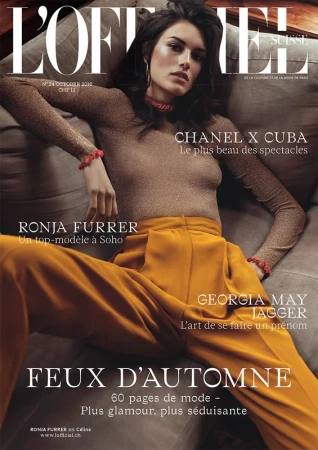 Model seated on a plush grey sofa wearing a metallic gold long-sleeve top and mustard yellow trousers.