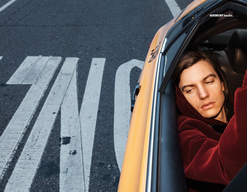 Adult male in a taxi with a burgundy hoodie, looking to the side with an urban street view through the front window.