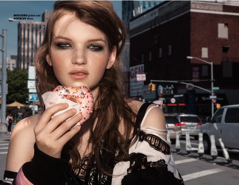 Young woman poses on a street with a sprinkle donut, wearing a Moschino jacket and Givenchy dress in an editorial fashion shot.