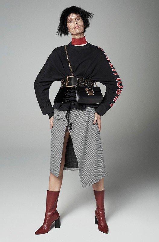 Fashion model posing in a studio wearing a black top, grey skirt, red boots and black purse with a red turtleneck under the top.