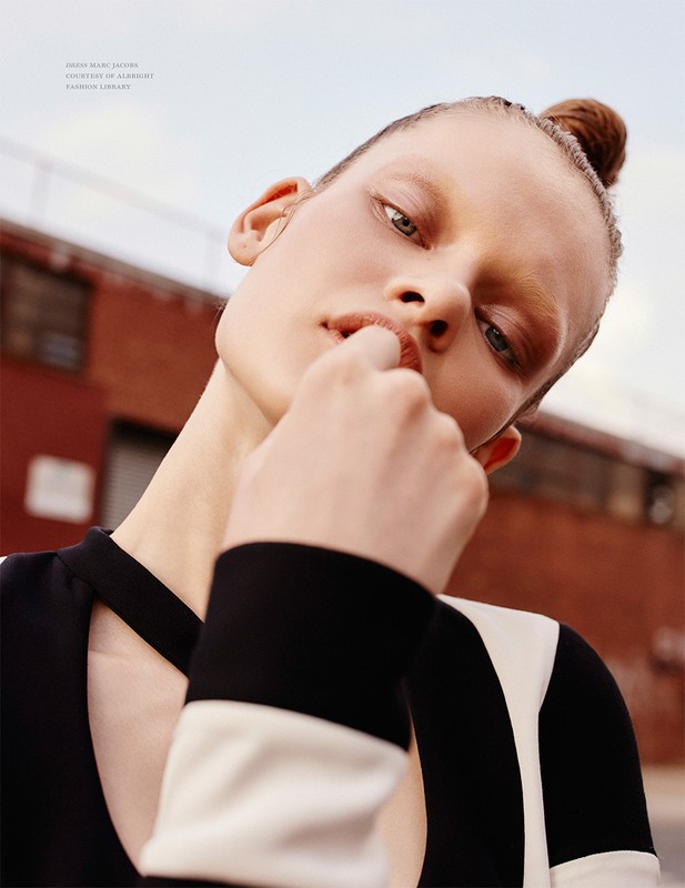 Fashion portrait of a woman with hair in a bun, wearing a black-and-white dress against an urban brick building under a bright sky.