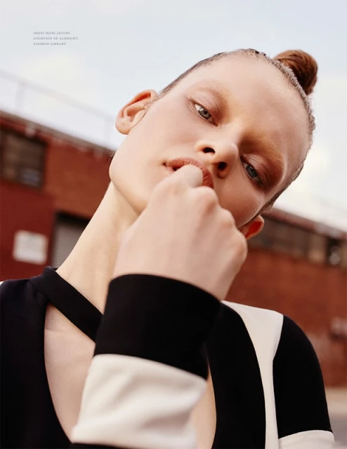 Fashion portrait of a woman with hair in a bun, wearing a black-and-white dress against an urban brick building under a bright sky.