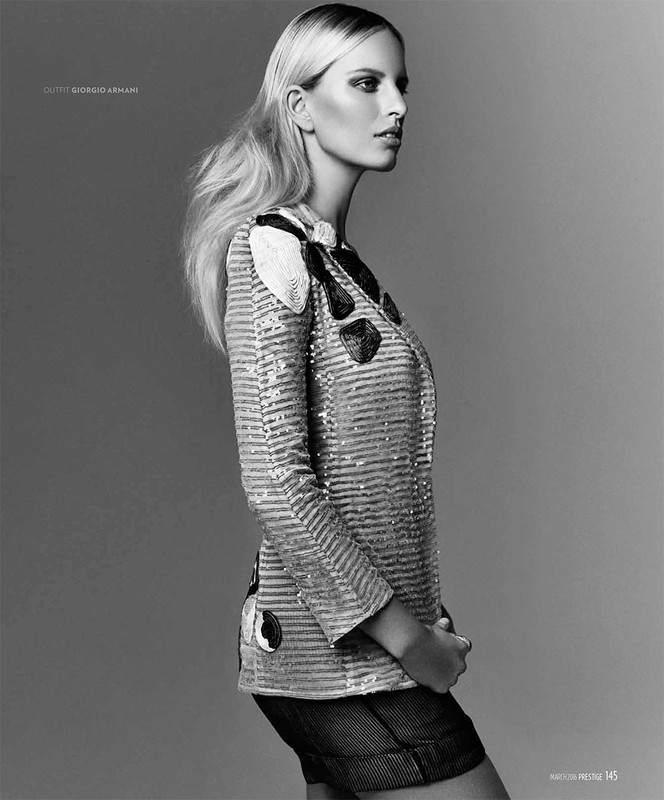 Black and white portrait of a blonde woman in a sequined jacket and shorts, posing against a plain grey studio background, fashion photography.