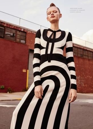 Model in a long black and white patterned dress standing outside against a red brick building and street in Los Angeles.