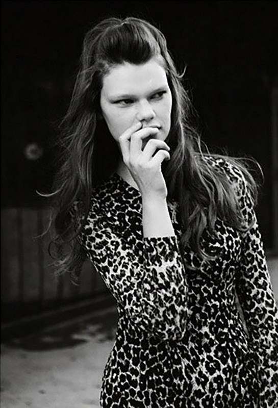 Monochrome portrait of a woman with long hair wearing a leopard print dress, with hand near face.