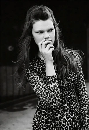 Monochrome portrait of a woman with long hair wearing a leopard print dress, with hand near face.