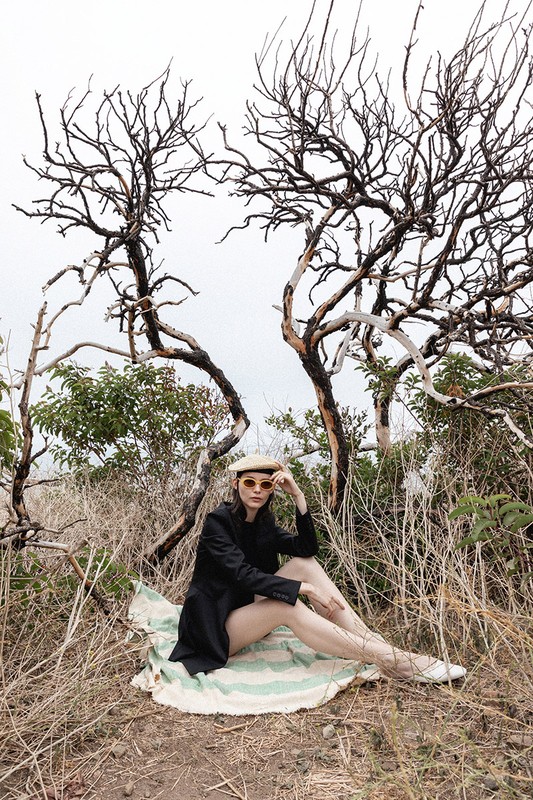 A seated woman wearing a black jacket and beret on a patterned blanket outdoors under bare trees styled by Steph Ashmore