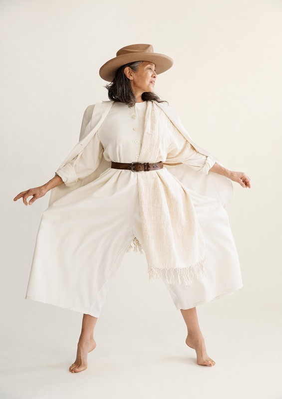 Older woman wearing a cream jumpsuit and hat styled by Steph Ashmore against a seamless white background.