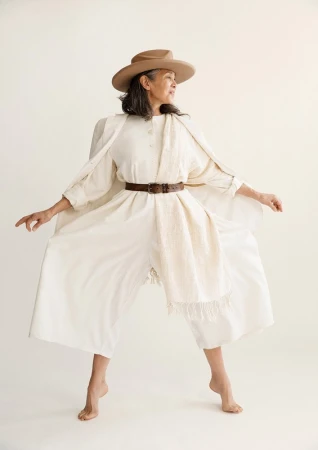 Older woman wearing a cream jumpsuit and hat styled by Steph Ashmore against a seamless white background.