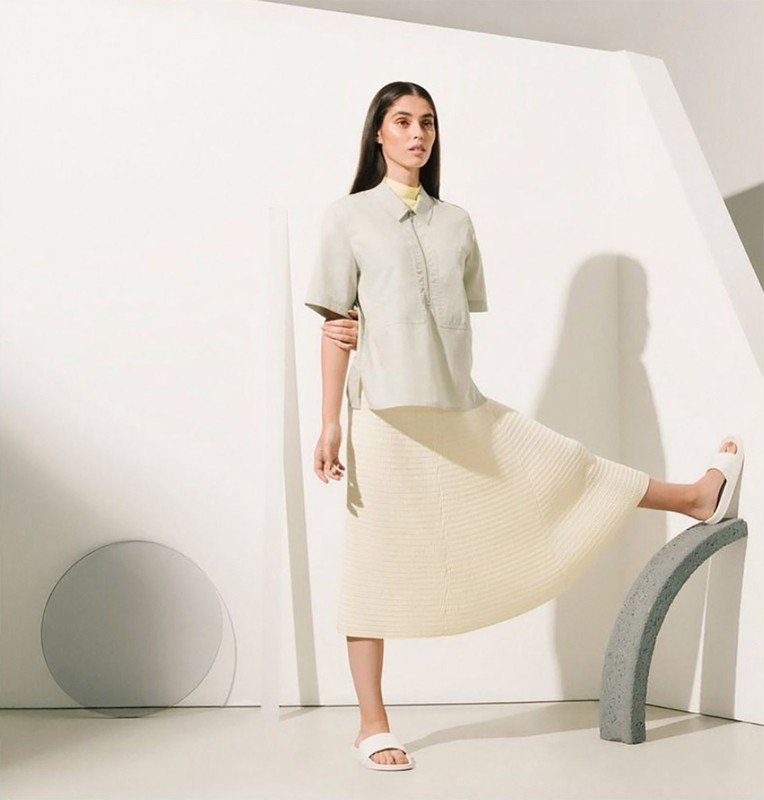 Adult woman poses in fashion shot wearing matching mint-green short-sleeve button-up shirt and cream-colored skirt in a photo studio.