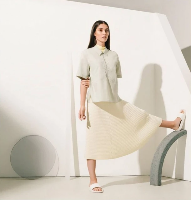 Adult woman poses in fashion shot wearing matching mint-green short-sleeve button-up shirt and cream-colored skirt in a photo studio.