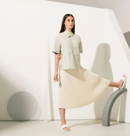 Adult woman poses in fashion shot wearing matching mint-green short-sleeve button-up shirt and cream-colored skirt in a photo studio.