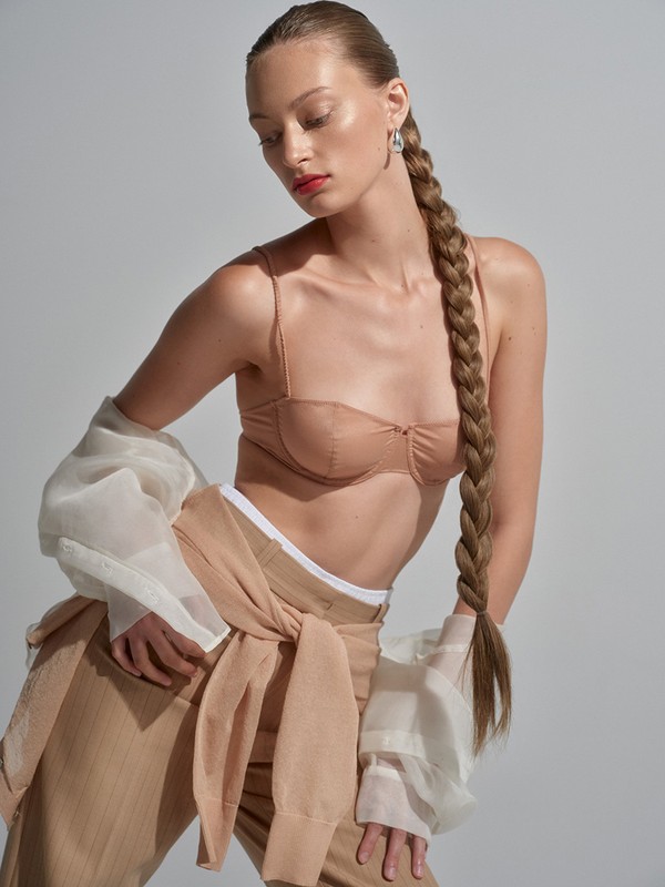 Model with long braid wearing nude bra top and tan trousers styled by Steph Ashmore against white seamless background