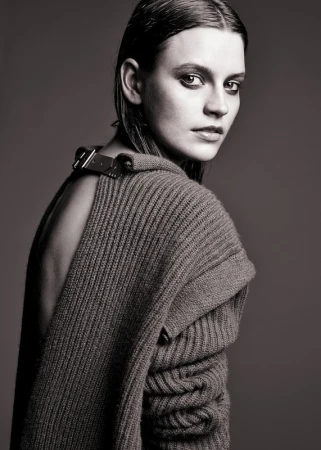 Portrait of a young woman with wet-look hair wearing a dark sweater, gazing over her shoulder in a studio setting.