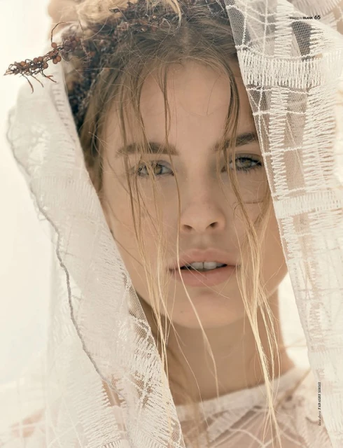 Close-up portrait of an adult female wearing a white, patterned lace veil and floral headdress with wet hair and soft, diffused lighting.