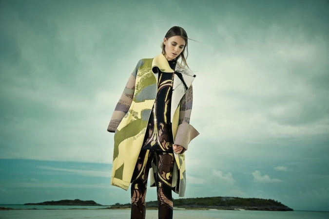 Model standing outdoors wearing a patterned coat and matching leggings under a cloudy sky.
