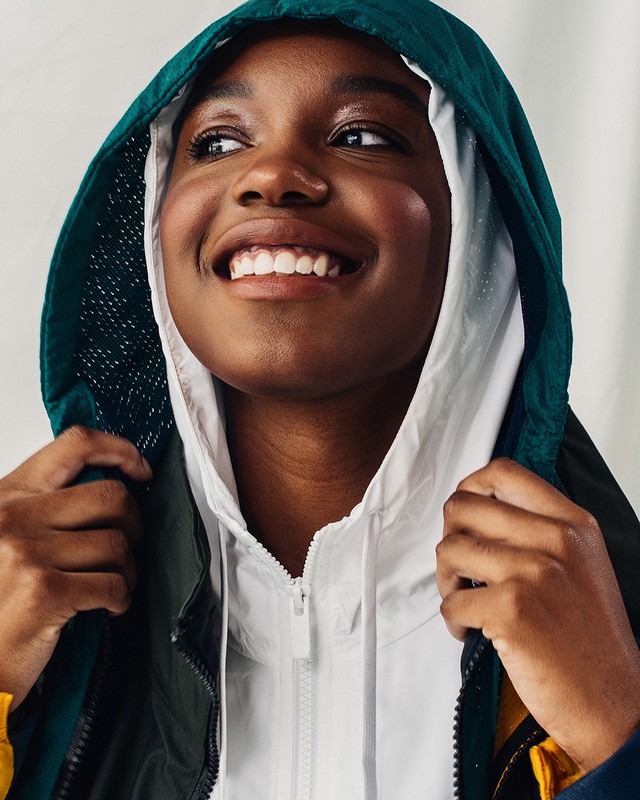 Close-up of an African-American woman wearing hooded jackets, smiling slightly, and looking to the upper left, against a neutral background.