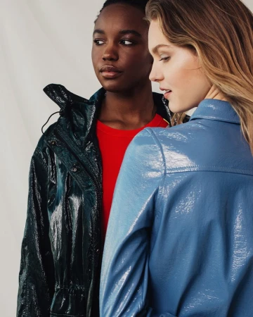 Two female models posing with glossy patent coats against a white backdrop in Los Angeles.