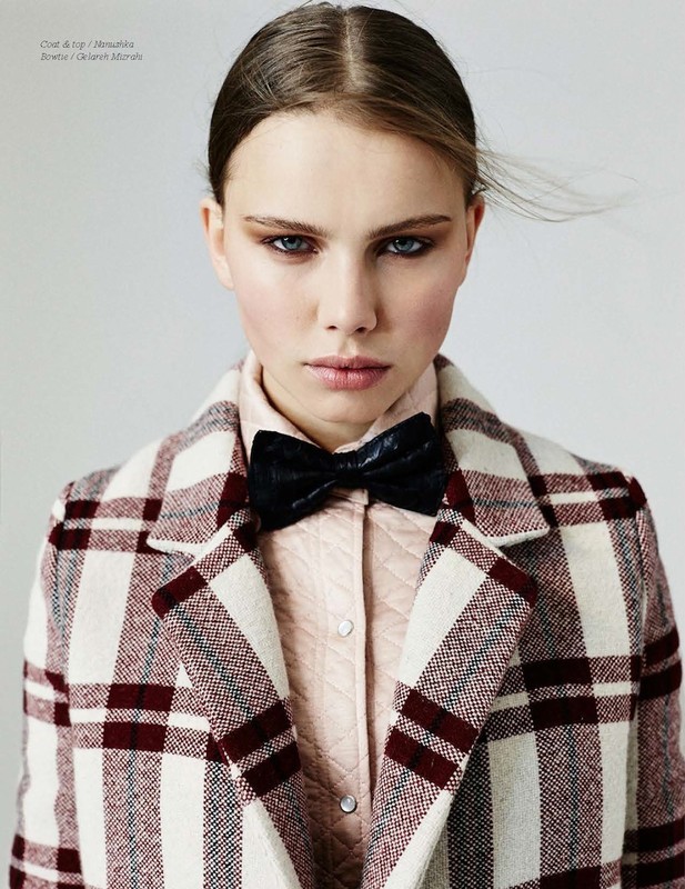 Close-up of a young adult woman wearing a plaid coat and bow tie looking at the camera in a studio environment with neutral background.