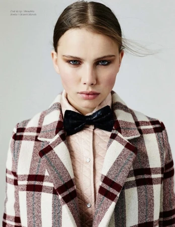 Close-up of a young adult woman wearing a plaid coat and bow tie looking at the camera in a studio environment with neutral background.