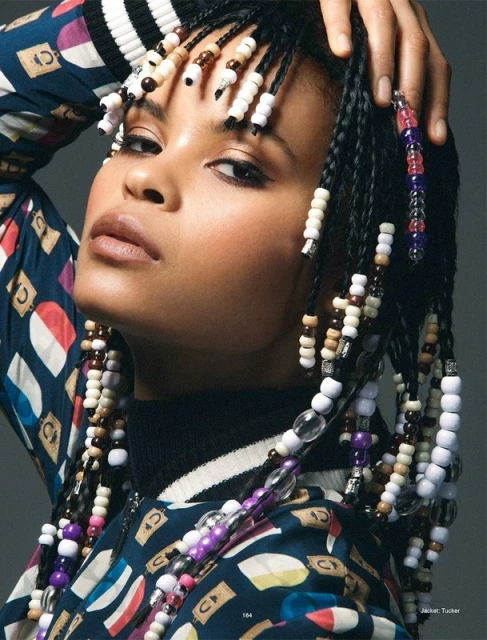 Portrait of a woman with beaded braids wearing patterned jacket against a gray backdrop. Beauty shot with fashion and style.