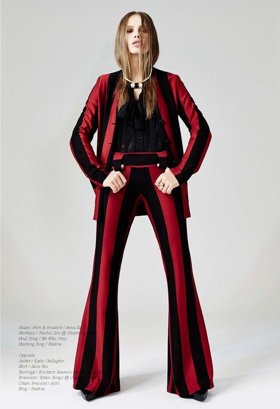 Fashion model in a red and black striped suit poses in a studio. Full-length shot of a woman with long hair wearing vintage-style clothing.