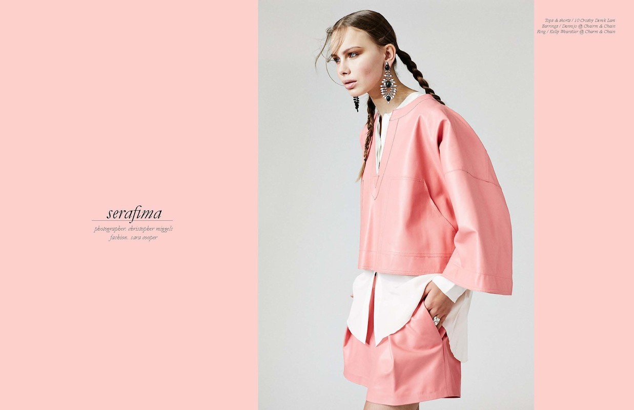 Fashion editorial shot: a fair-skinned woman with braided hair poses in a pink skirt and matching pink top. She wears large statement earrings.