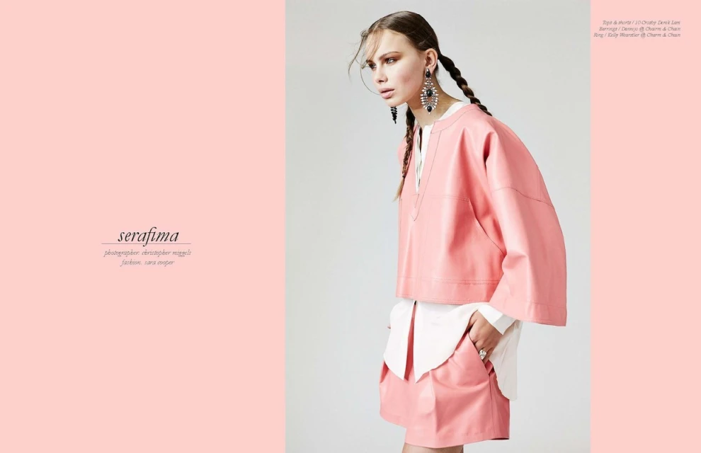 Fashion editorial shot: a fair-skinned woman with braided hair poses in a pink skirt and matching pink top. She wears large statement earrings.