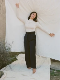 Woman in cream top and black trousers standing against draped white fabric in Los Angeles, styled by Stephanie Peterson.