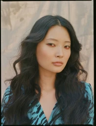 Portrait of an East Asian woman with long dark wavy hair wearing a bright blue and black patterned top