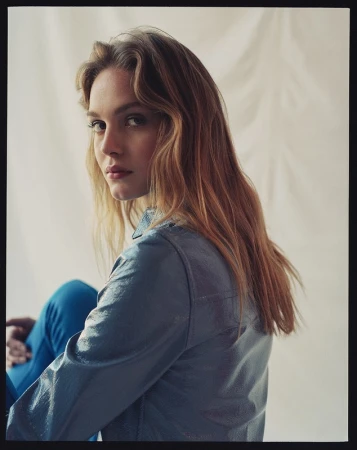 Portrait of a woman with long blonde hair wearing a blue jacket against a draped fabric background.