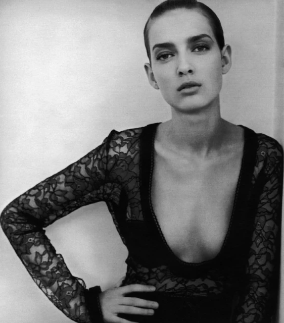 Black and white portrait of a poised woman wearing a lace top, set against a neutral backdrop in a studio-style setting.