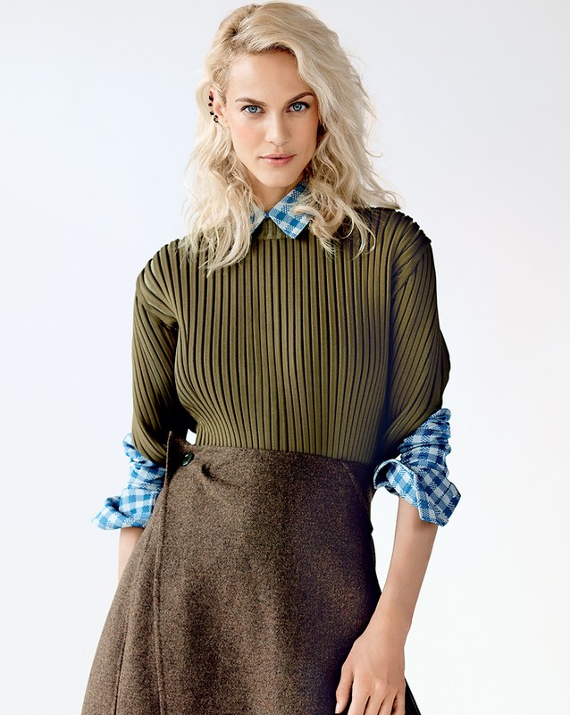 Fashionable woman in olive green top and brown skirt poses in a studio. Portrait of a female model in stylish clothing.