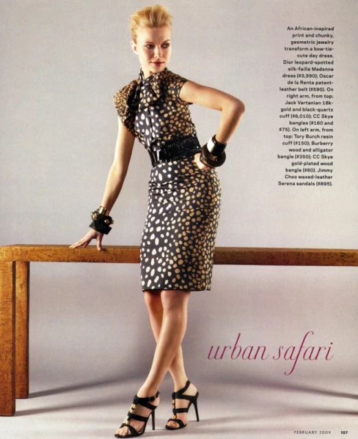 Fashion editorial shot of a blond woman wearing a spotted black and brown dress with statement black jewelry and sandals in a studio.