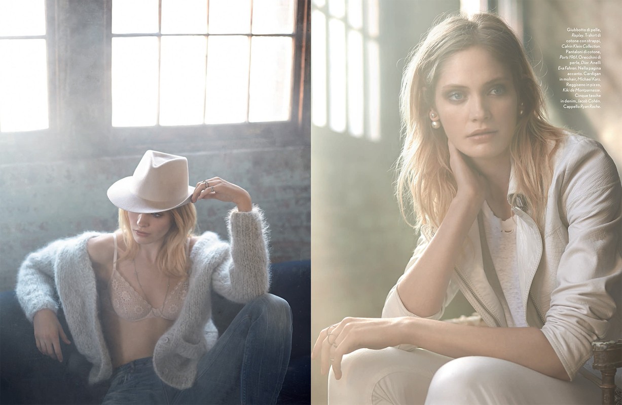 Fashionable adult woman posing indoors wearing a hat, jeans, and a cardigan sweater, while a second woman is seated in a jacket.