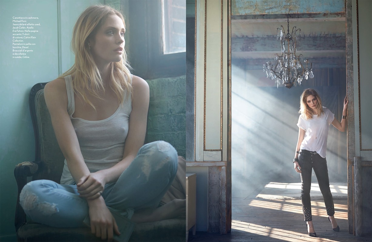 Blonde woman in a white tank top and jeans seated in an armchair by a window; a woman in black pants by a chandelier.