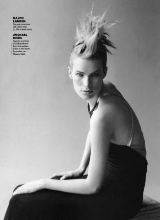 Monochrome portrait of a female model with an elaborate spiky updo hairstyle, wearing a dark dress with straps.
