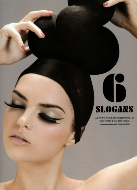 Close-up portrait of a woman with dramatic makeup and a black headpiece, hands adjusting it; studio shot for beauty or fashion.
