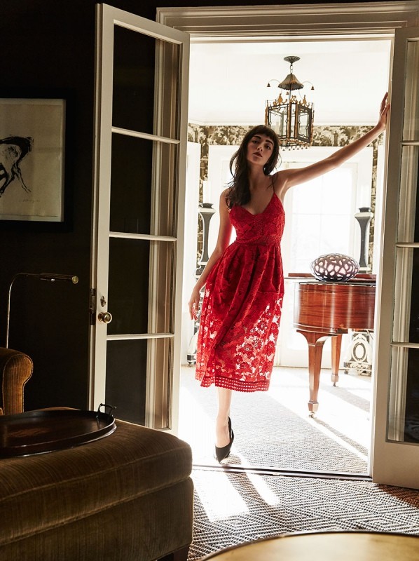Elegant woman poses in a red lace dress within a doorway, framed by interior design details, warm lighting, and classic architectural elements.