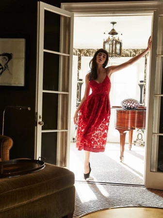 Elegant woman poses in a red lace dress within a doorway, framed by interior design details, warm lighting, and classic architectural elements.