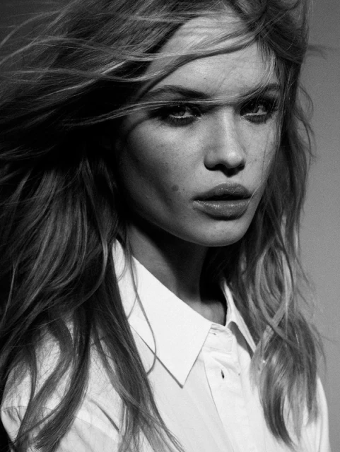 Black and white portrait of a blonde adult female looking at the camera wearing a white button-down shirt and wavy hair.