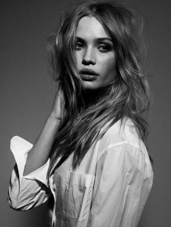 Black and white portrait of a woman with tousled blonde hair wearing an unbuttoned white shirt against a neutral background